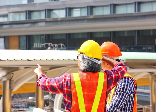 Dois trabalhadores de roupa de segurança estão olhando para o local de construção