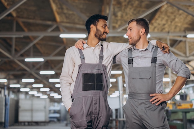 Dois trabalhadores internacionais felizes de macacão se abraçam contra um fundo de fábrica