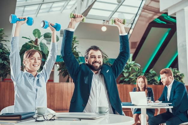 Dois trabalhadores que exercitam com pesos na mesa no escritório.