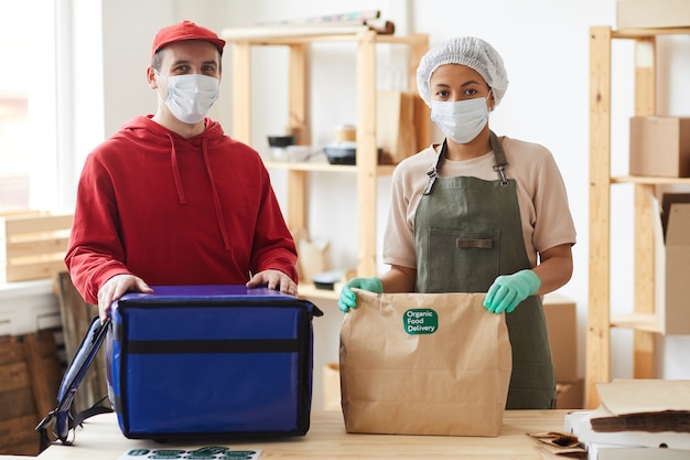 Foto dois trabalhadores usando máscaras enquanto embalam pedidos em um serviço de entrega de comida sem contato