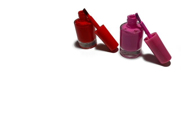 Foto dois tubos abertos de esmalte em pé sobre uma mesa branca. o esmalte é vermelho e rosa.
