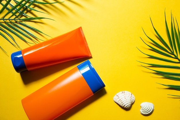 Dois tubos com protetores solares simulados em um fundo amarelo de verão. Proteção UV da pele com filtro FPS, shampoo e condicionador para os cabelos. Um bronzeado seguro na praia. Flat lay - resort no mar.
