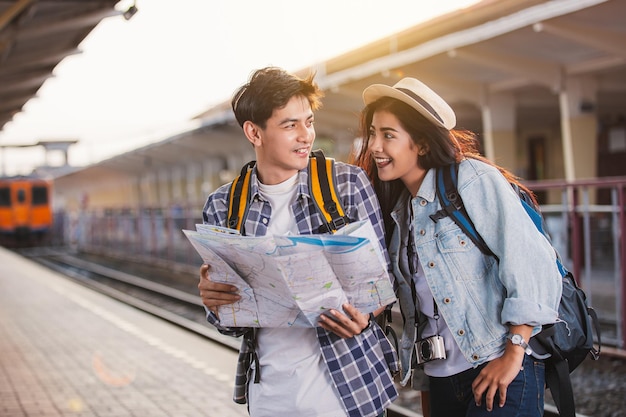 Dois turistas asiáticos com mochilas viajam na estação de trem com um viajante, estilo vintage.