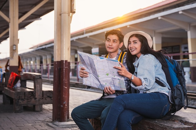 Dois turistas asiáticos com mochilas viajam na estação de trem com um viajante, estilo vintage.