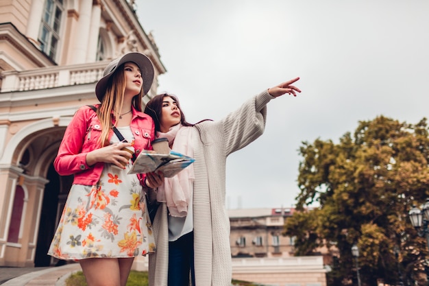 Dois turistas das mulheres que procuram pela maneira direita usando o mapa em Odessa. Felizes amigos viajantes mostrando direção