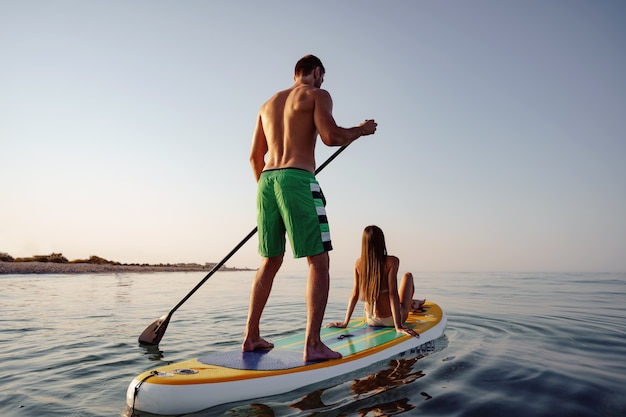 Dois turistas, jovem e mulher, se divertindo com o paddleboarding no mar