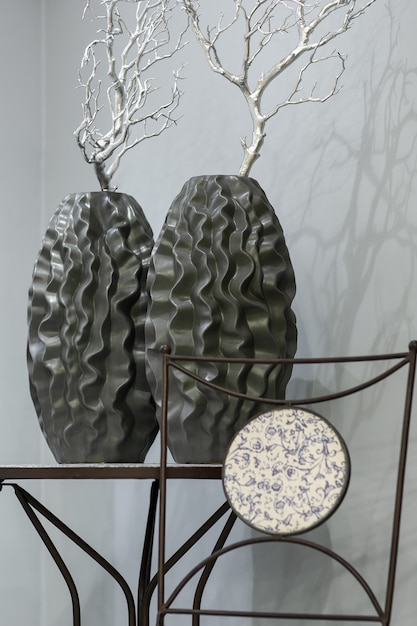 Dois vasos escuros com curvas e um galho de prata sobre a mesa contra o fundo de uma parede cinza