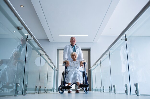 Doktor, der älteren Patienten auf Rollstuhl im Durchgang hält