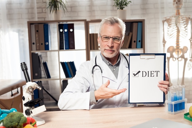 Doktor, der am Schreibtisch in der Klinik mit Mikroskop sitzt.