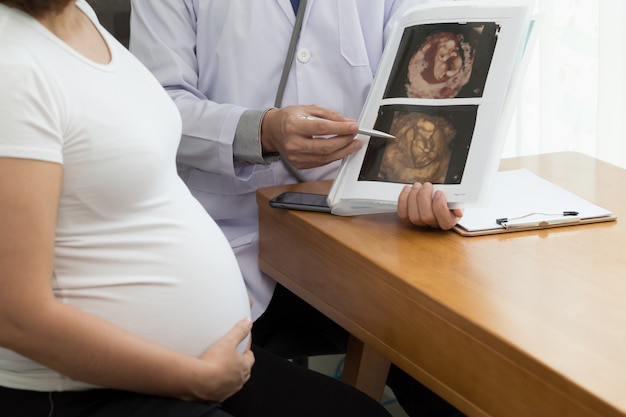 Doktor, der Bildergebnis des Ultraschalls 4D hält und mit der schwangeren Frau spricht. Während der Schwangerschaft Konzept