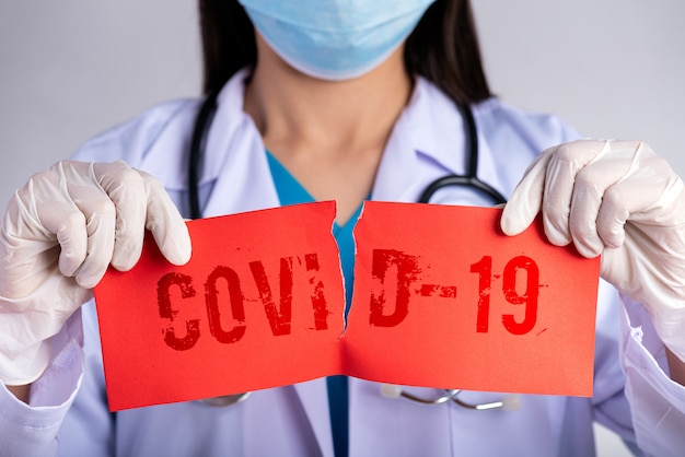 Foto doktor, der chirurgische maske, stethoskop trägt und rotes zerrissenes papier mit covid-19-text hält