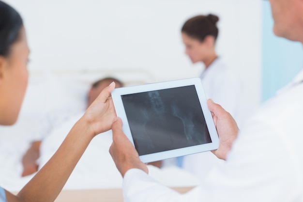 Foto doktor, der digitale tablette mit kollegen und patienten hinten verwendet