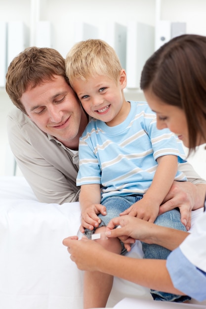 Doktor, der einen Gips auf dem Knie eines lächelnden Jungen anwendet