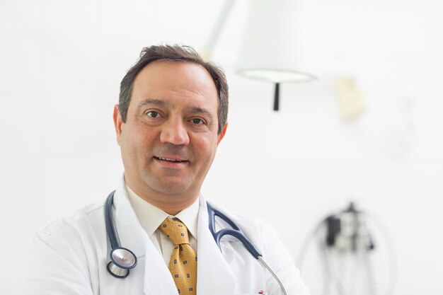 Doktor, der mit einem stethoskop um seinen hals in einem prüfungsraum lächelt