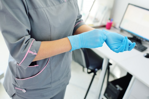 Doktor eine Frau bereitet sich auf einen medizinischen Termin oder eine Operation vor, indem sie Gummihandschuhe vor dem Hintergrund einer modernen Klinik trägt.