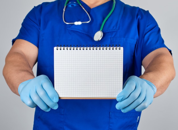 Doktor in den blauen einheitlichen und sterilen Latexhandschuhen, die offenes leeres Notizbuch halten