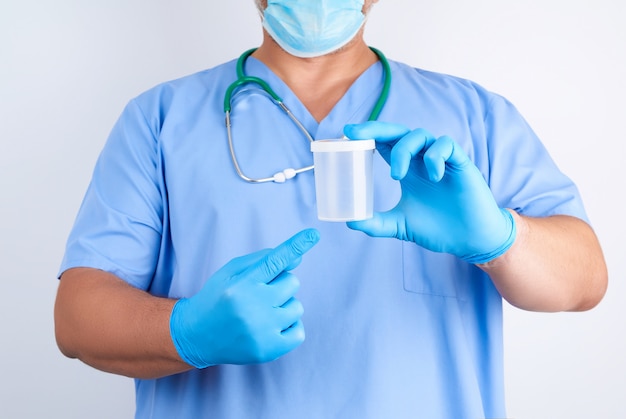 Doktor in der blauen Uniform, die einen leeren Plastikbehälter für die Entnahme von Urinproben hält