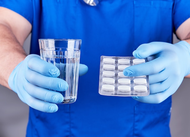 Doktor in der blauen Uniform hält ein Glas Wasser und eine Packung Pillen