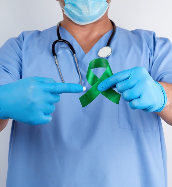 Doktor in der blauen Uniform und in den Latexhandschuhen hält ein grünes Band als Symbol der frühen Forschung und der Krankheit