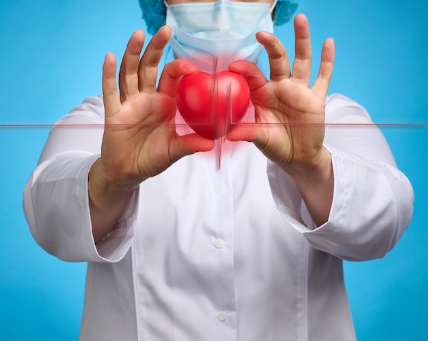 Foto doktor in einem weißen medizinischen kittel, der ein rotes herz hält. herz-kreislauf-krankheitskonzept, früherkennung. blauer hintergrund