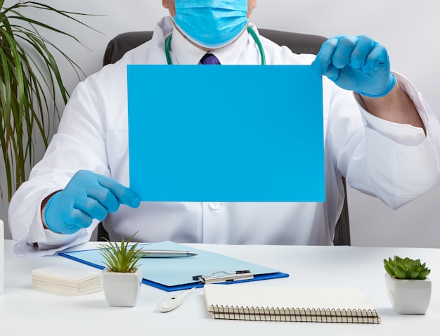 Doktor in einem weißen medizinischen Mantel sitzt an einem Tisch in einem braunen Ledersessel und hält ein leeres blaues Blatt Papier