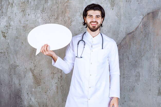 Doktor mit einem Stethoskop, das eine ovale leere Infotafel hält.