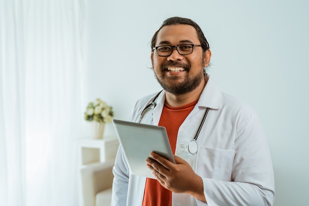 Doktor mit Tablet-PC in seinem Büro und lächelnd