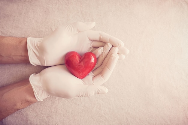 Doktorhände mit Handschuhen, die rotes Herz, Krankenversicherung, Spendenkonzept halten