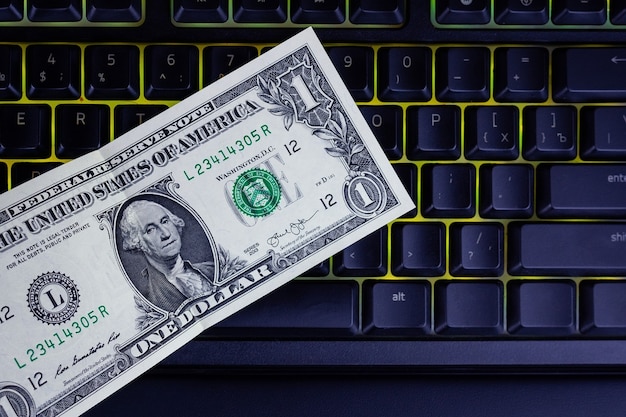 Un dólar se encuentra en un teclado retroiluminado negro, dólar y fondo de teclado, concepto de negocio