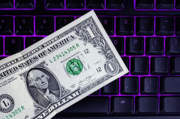 Un dólar se encuentra en un teclado retroiluminado negro, dólar y fondo de teclado, concepto de negocio