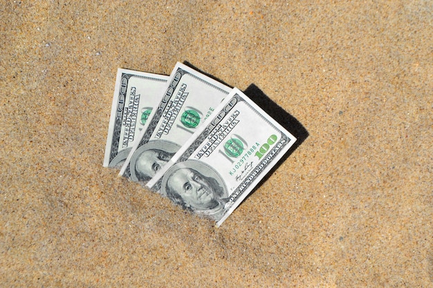 Dólares de dinero medio cubierto con arena se encuentran en la playa de cerca