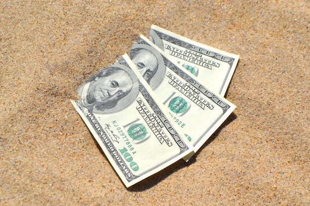 Dólares de dinero medio cubiertos con arena se encuentran en primer plano de la playa