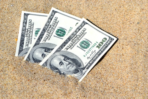 Dólares de dinero medio cubiertos con arena se encuentran en primer plano de la playa