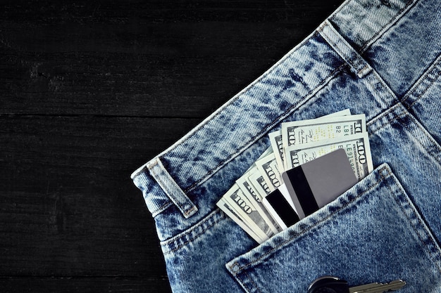 Dólares e cartões em seu bolso jeans em fundo preto de madeira