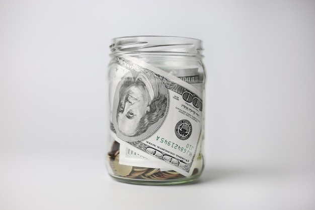 Dólares em uma jarra de vidro com moedas em um fundo branco. Conceito de economia de dinheiro