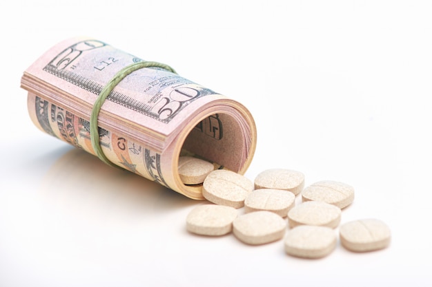 Dólares envueltos y píldoras medicinales sobre blanco