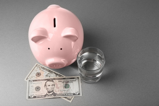 Foto dólares de hucha rosa y vaso de agua sobre fondo gris concepto de ahorro de agua