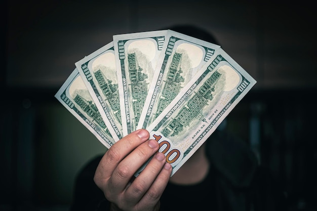 Dólares en las manos Empresario con camisa azul sosteniendo un abanico de dinero de 500 dólares