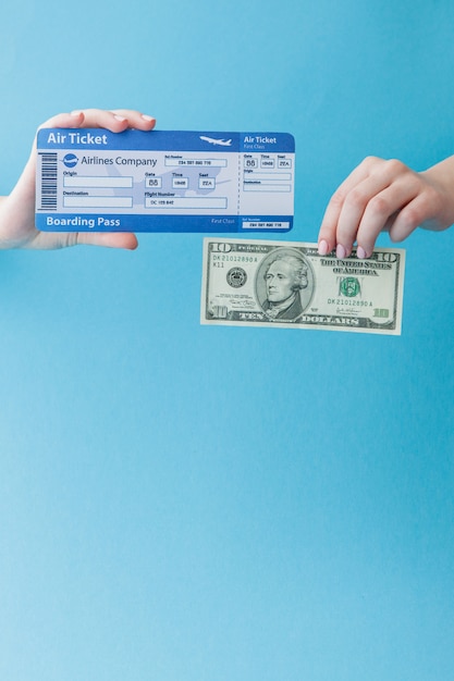 Dollar und Flugticket in der Frauenhand auf einem blauen Hintergrund. Reisekonzept, Kopierraum