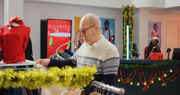 Dolly en una toma de un cliente sénior en una tienda de un centro comercial adornado festivo tratando de determinar si un blazer elegante le queda bien.