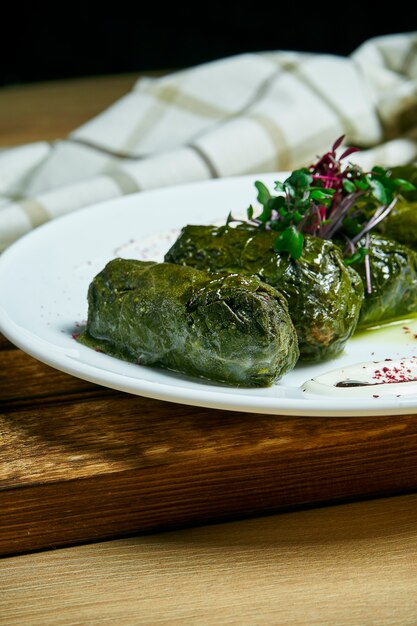 Dolma georgiano tradicional en hojas de parra con arroz y carne en un plato blanco sobre mesa de madera.