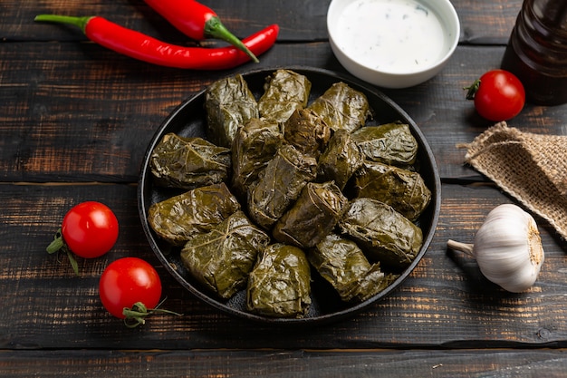 Foto dolma oder tolma oder sarma gefüllte weinblätter mit reis und fleisch auf holzhintergrund. traditionelle kaukasische, osmanische, türkische und griechische küche