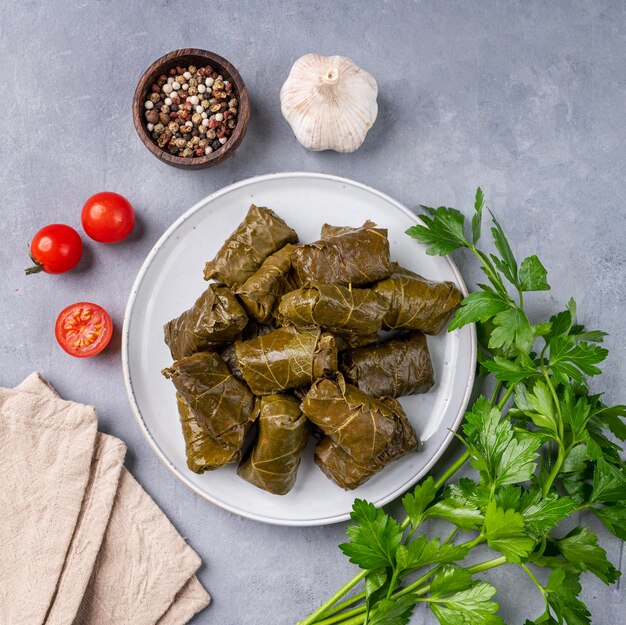 Dolma recheado de uva deixa a tradicional cozinha grega turca caucasiana em um prato azul com ervas frescas sobre um fundo claro com tomate, alho e pimenta