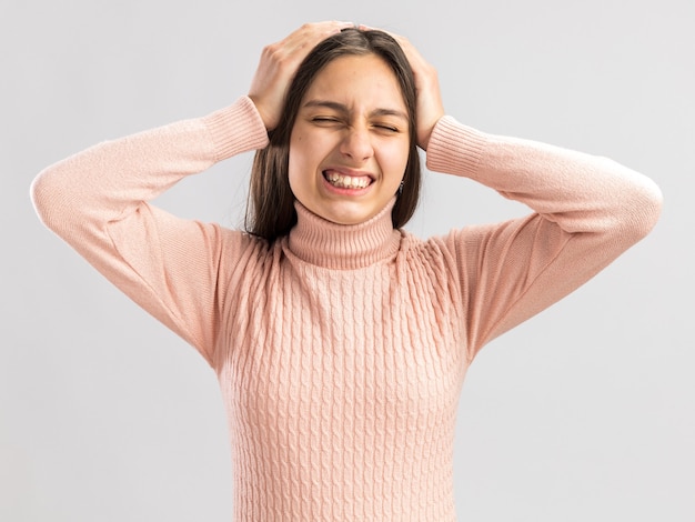 Dolor bastante adolescente manteniendo las manos en la cabeza con los ojos cerrados aislado en la pared blanca