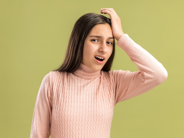 Dolor bastante adolescente mirando al frente manteniendo la mano en la cabeza con la boca abierta aislada en la pared verde oliva