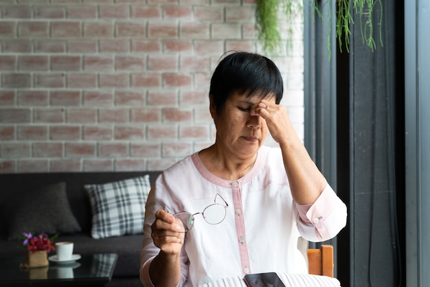 Dolor de cabeza de anciana mientras usa teléfono inteligente, cuidado de la salud