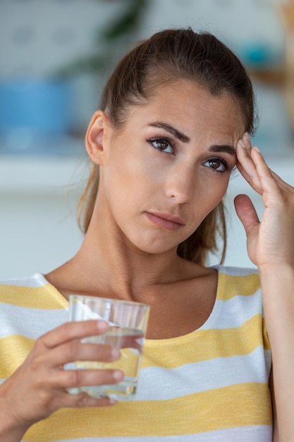 Dolor de cabeza Foto de cierre de una mujer joven que está sentada en un sofá tocándose la cabeza mientras sufre de migraña