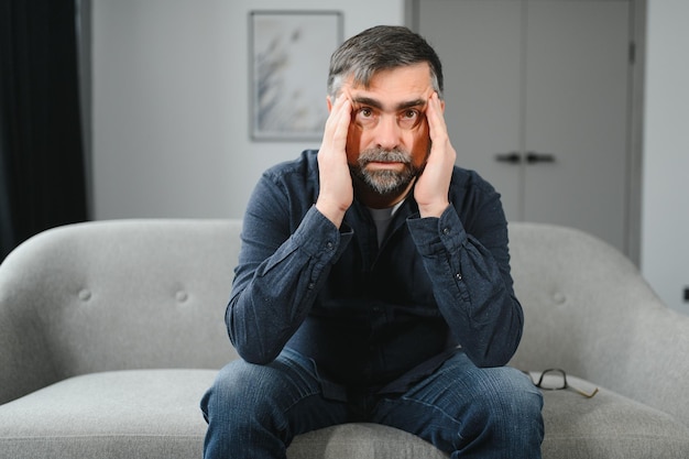 Foto dolor de cabeza hombre mayor que sufre de dolor de migraña masaje de templos sentado en el hogar problemas de salud de salud en el concepto de edad avanzada