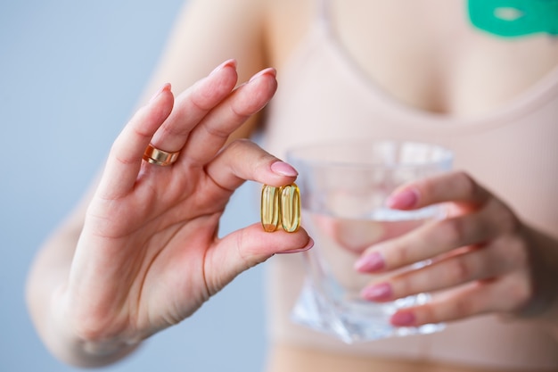 Dolor de cabeza, mano con pastillas. La mujer toma el medicamento con un vaso de agua. Valor diario de vitaminas, medicamentos efectivos, farmacia moderna para el cuerpo y el concepto de salud mental.