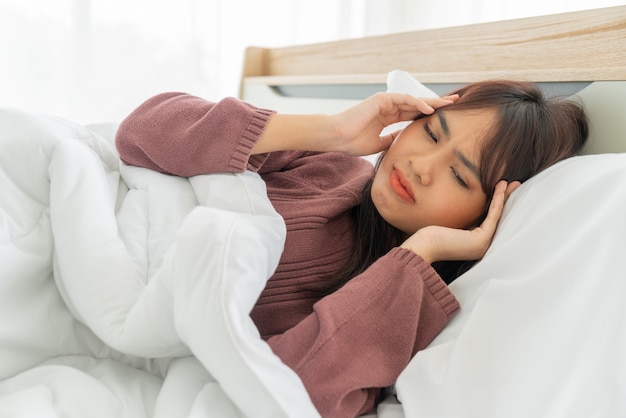 Foto dolor de cabeza de las mujeres asiáticas y dormir en la cama